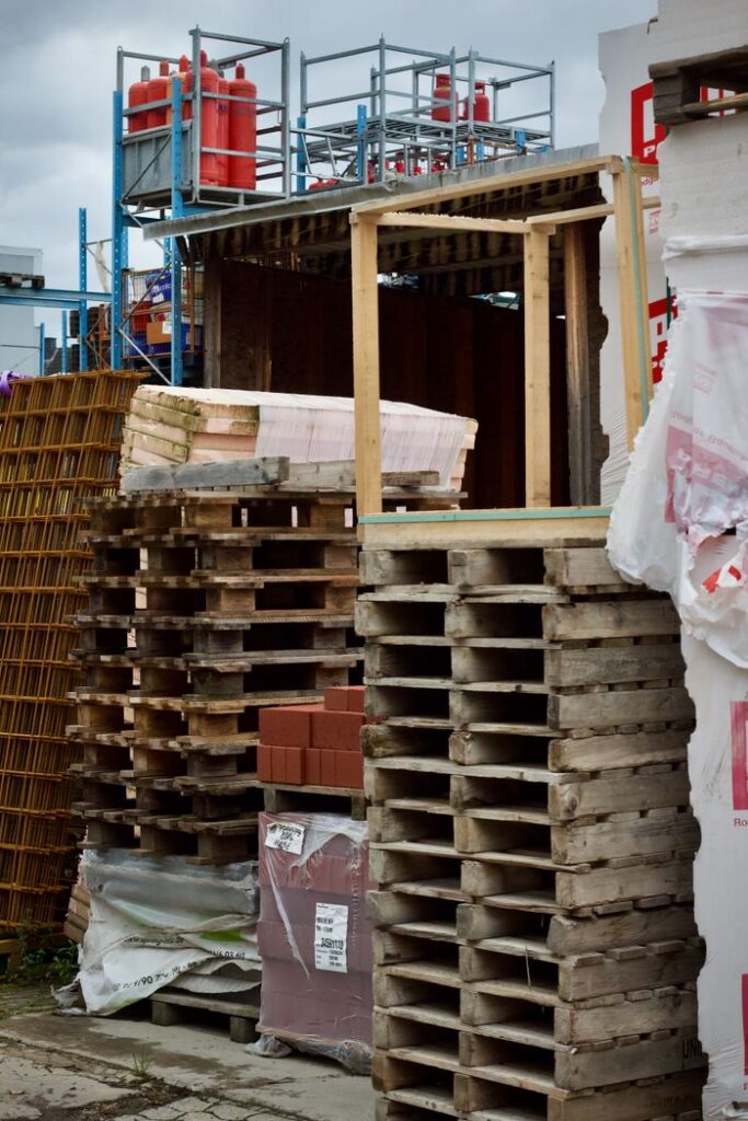 Wooden pallets stacked at an outdoor construction site amidst various building materials.